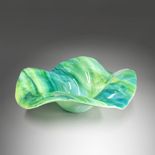 This stunning sculptured glass bowl captures the essence of the sea in every ripple and wave. Handcrafted in Cincinnati, Ohio, this exquisite bowl will elevate your beach house décor to a whole new level.The color palette of this fused glass wave bowl is reminiscent of the tranquil ocean waters. Sea blue and green hues…