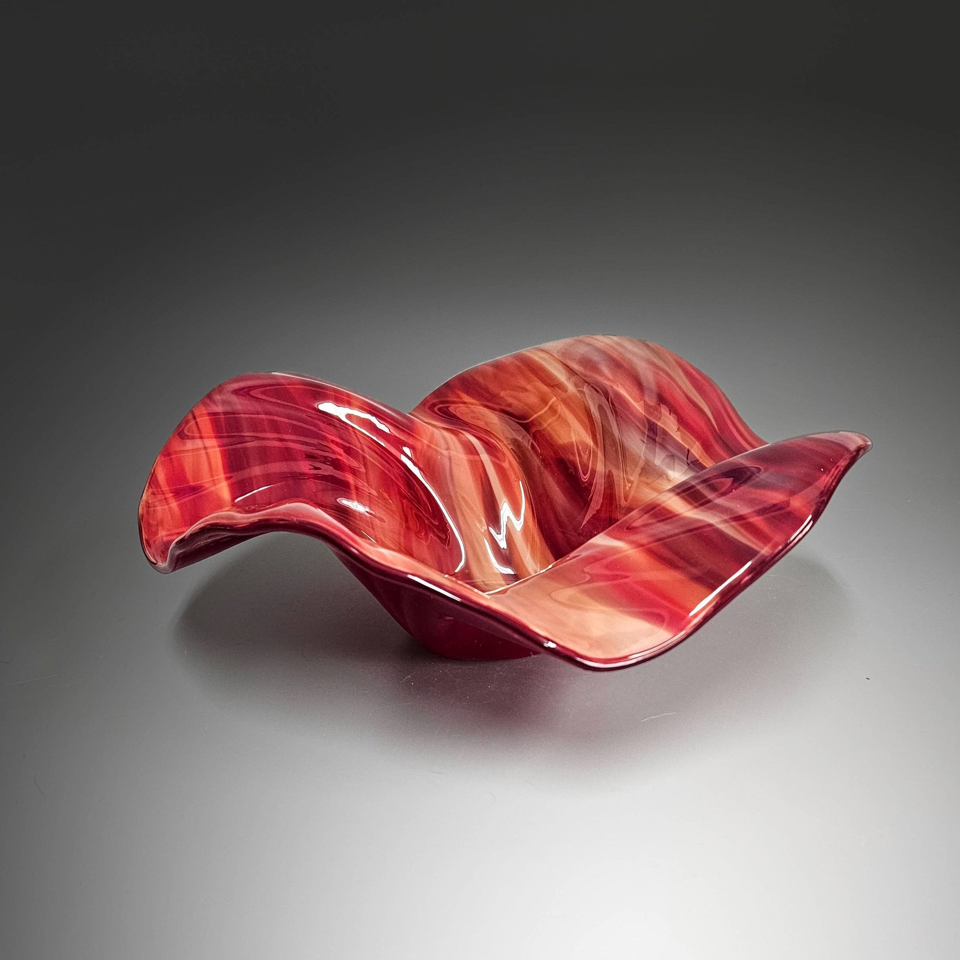 This beautiful glass wave bowl is done in striking mix of shaded reds.  It's done in a mix of transparent glass which lets the light play off the swirls in the glass beautifully. The color is stunning.